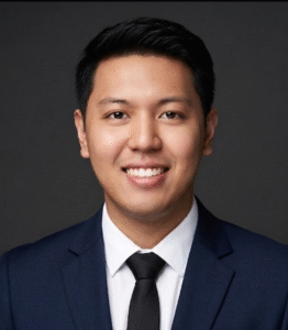 Square portrait of a smiling person in a suit and tie against a neutral background